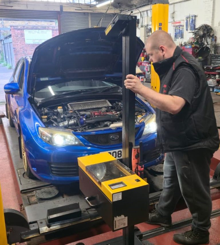 Great Customer Service A mechanic using equipment to inspect and align the headlights on a blue car with its bonnet open in a garage.
